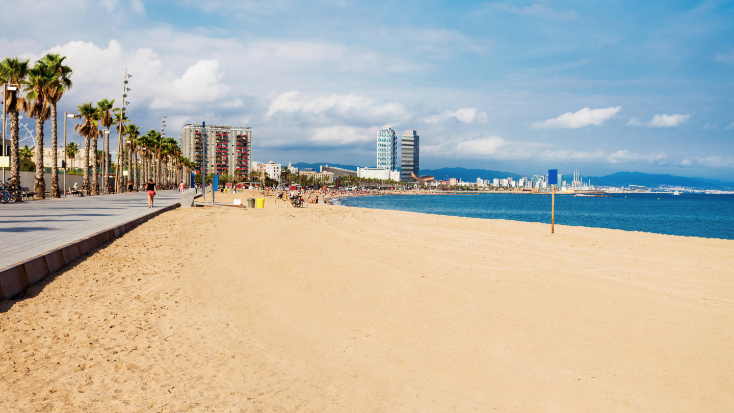 Der goldene Sandstrand von Barceloneta mit Blick auf das blaue Mittelmeer, Palmen und die charakteristische Skyline von Barcelona